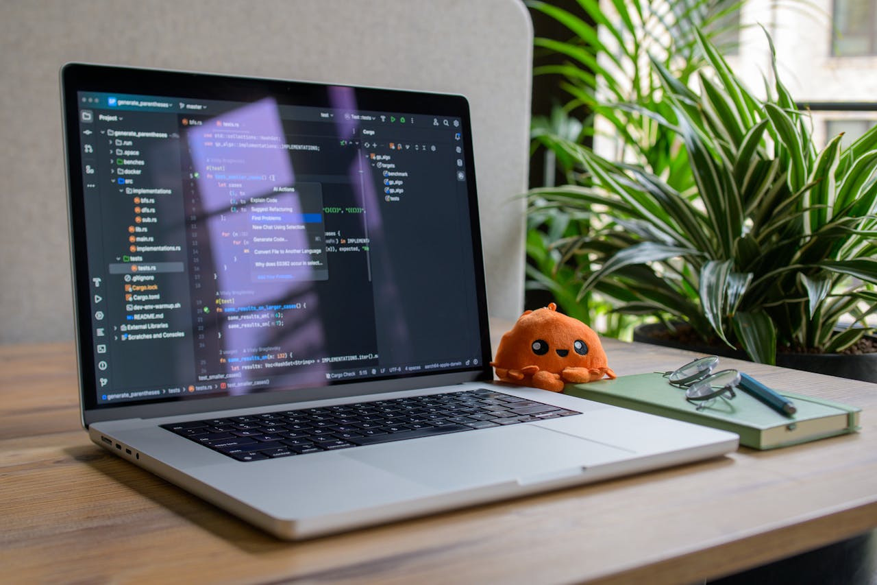Laptop with coding interface, plant, and toy for a cozy workspace vibe.
